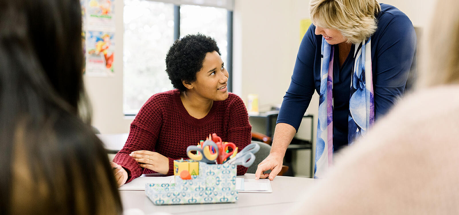 A professor leans over as she explains something to a student who is sitting