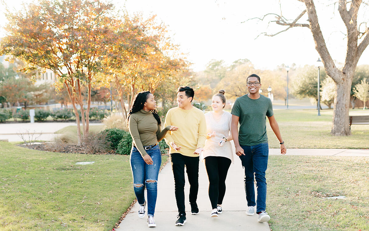 Four students walking on the sidewalks of campus together 
