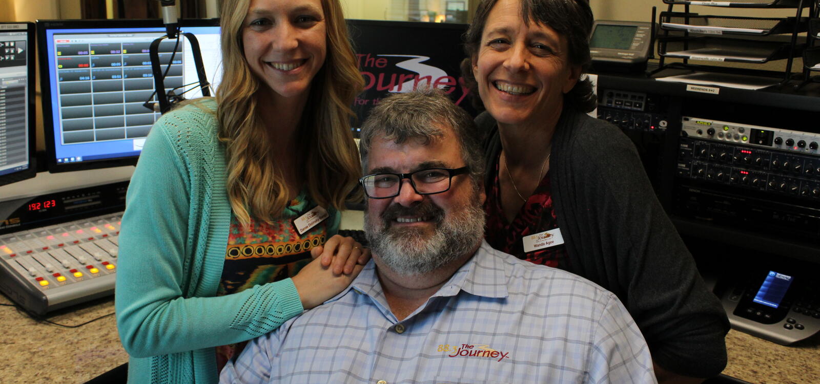 Danae Songy and Wanda Agee posing behind Mike Agee inside the radio station