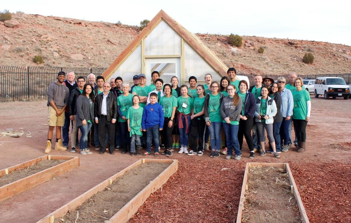 A group of people, most matching in green shirts, stand in front of a newly built greenhouse