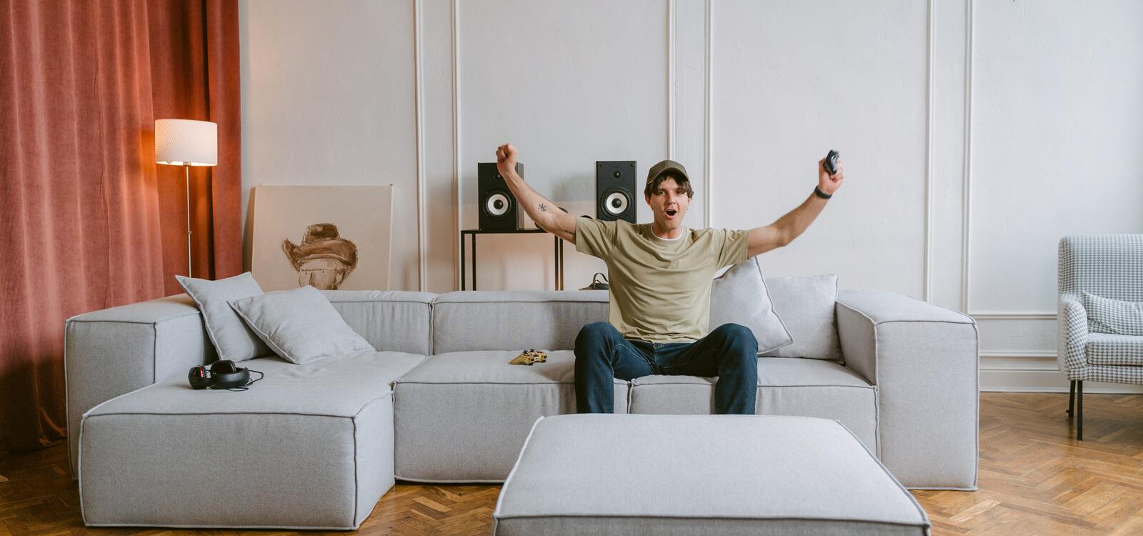 Man sitting on couch holding arms up in victory with a video game controller in hand