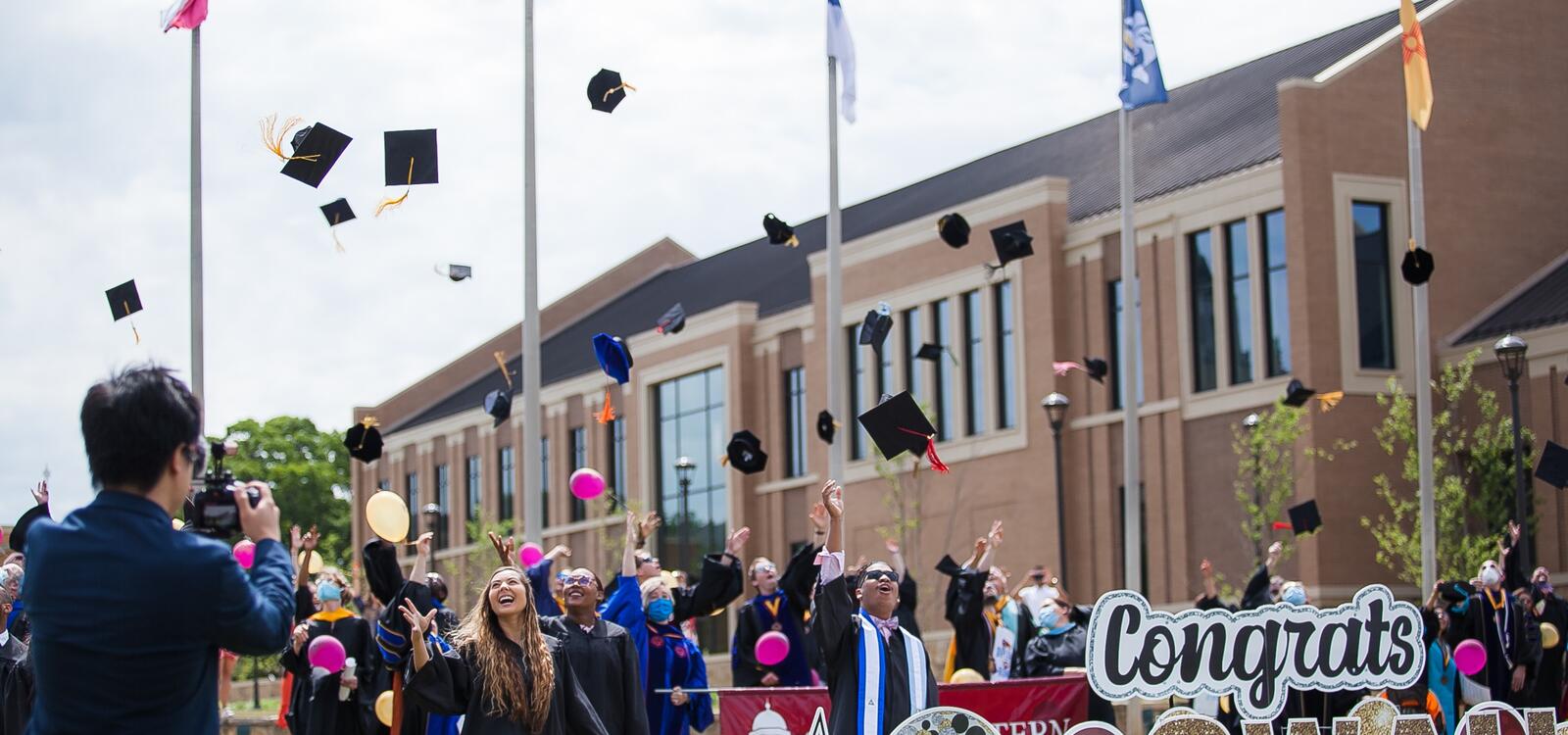 Graduating seniors throw their caps in the air while being surrounded by proud faculty and staff