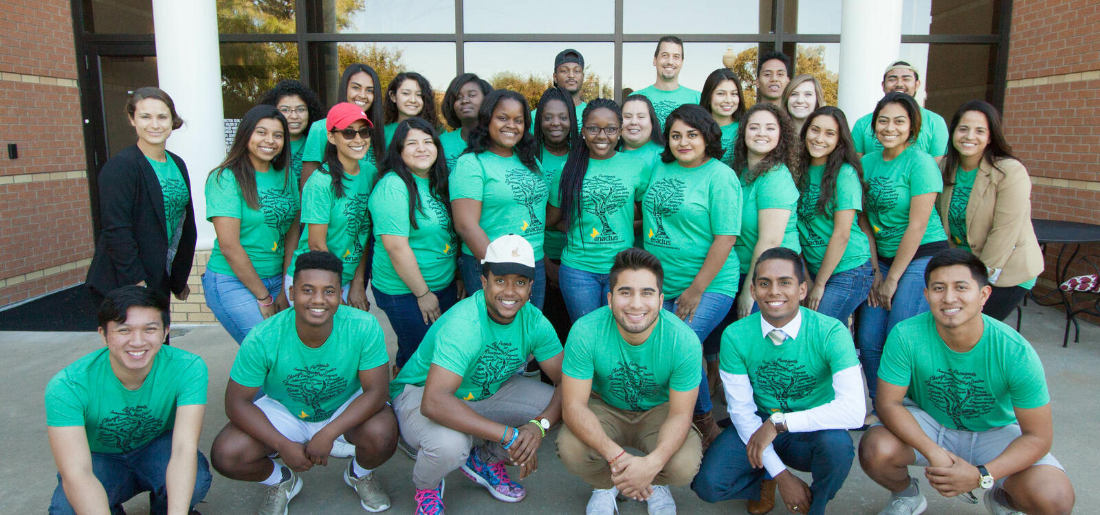 Dressed in matching green t-shirts, a group students stand in four rows and smile