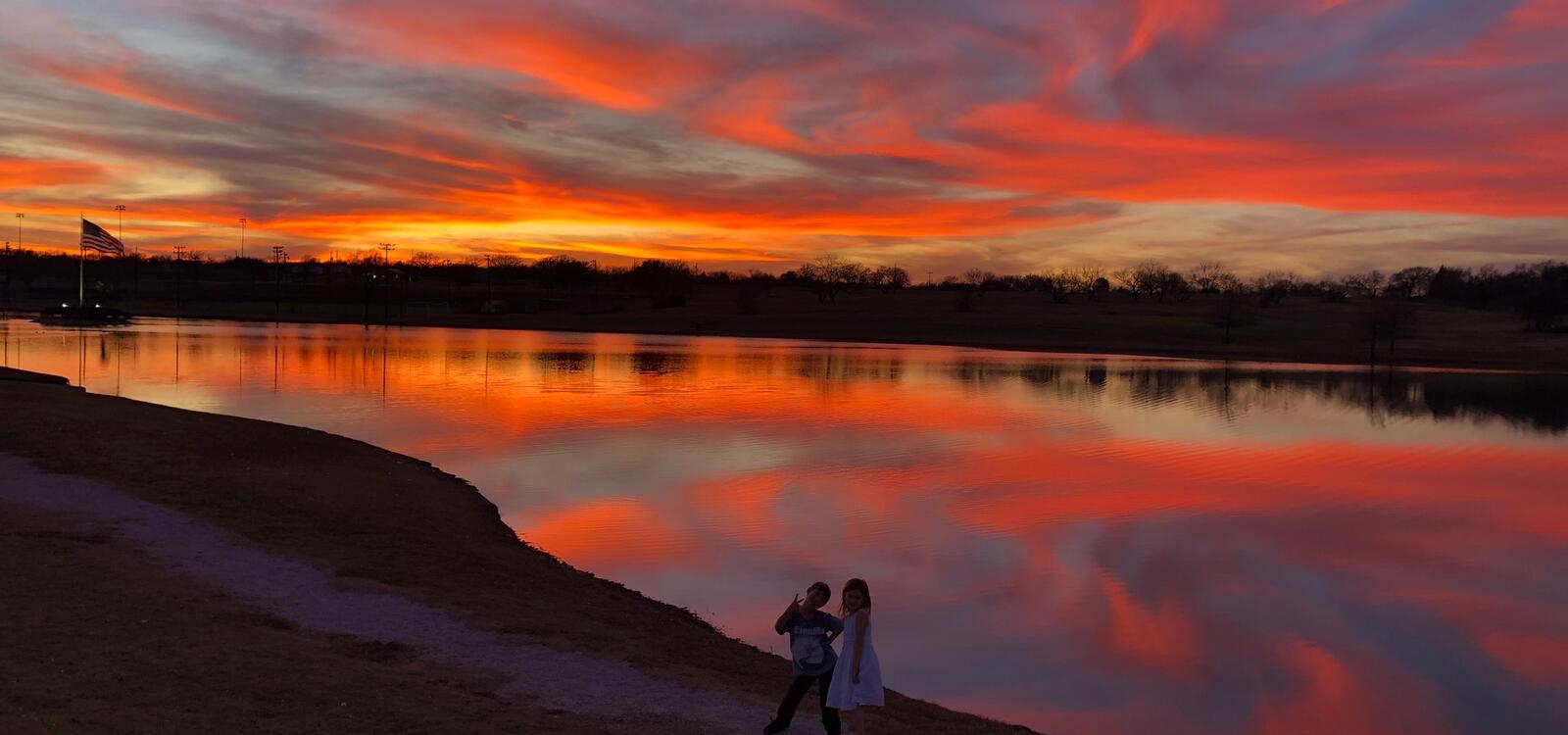 The sunset sets in pink, orange and blue colors and reflects off of the water of the duck pond