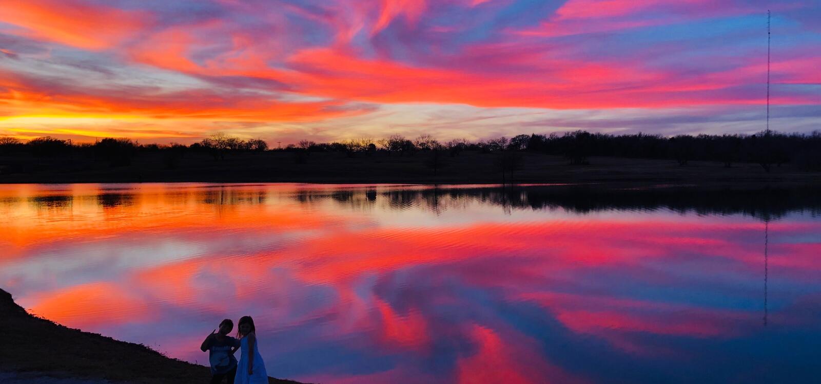 A beautiful sunset made up of blues, pinks, oranges and yellows reflect off of the pond's water