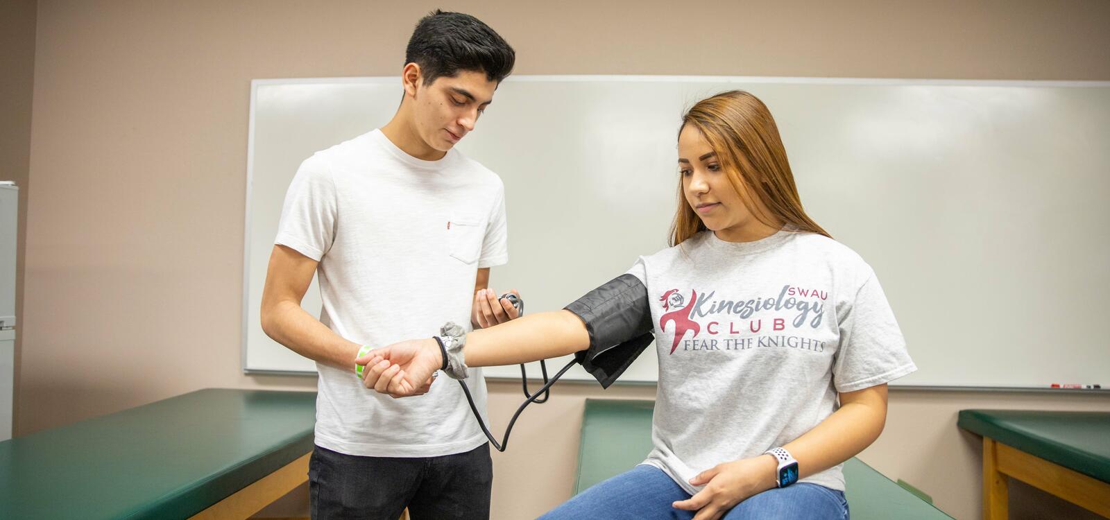 Two students in kinesiology building checking eachother's blood pressure.