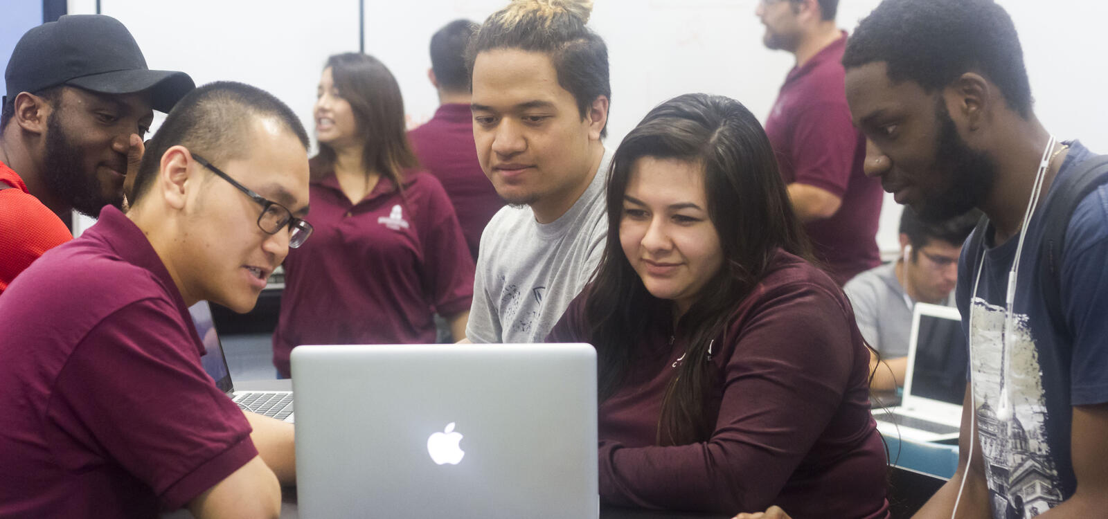 A CASA tutor looks at a laptop and tutors the three students in front of him