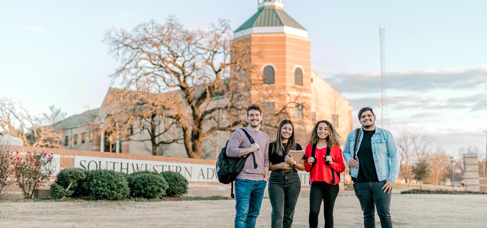 Four students, with backpacks, smile together as they stand in front of a bricked sign that reads " Southwestern Adventist University" 