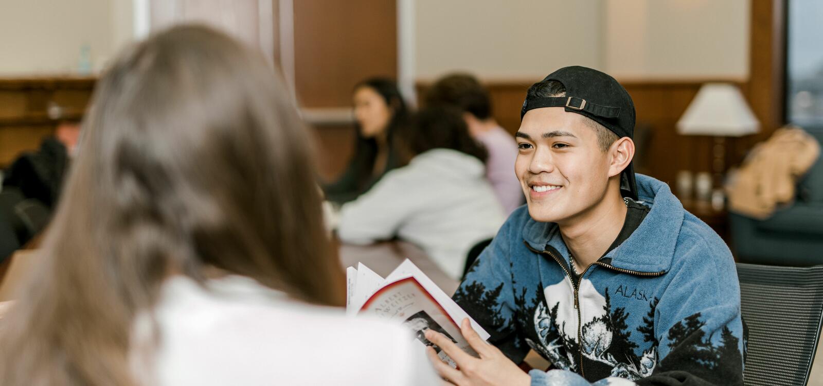 A student smiles as he talks to his peer sitting across from him