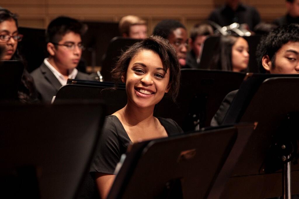A young student smiles as she sits among her peers waiting to practice their piece