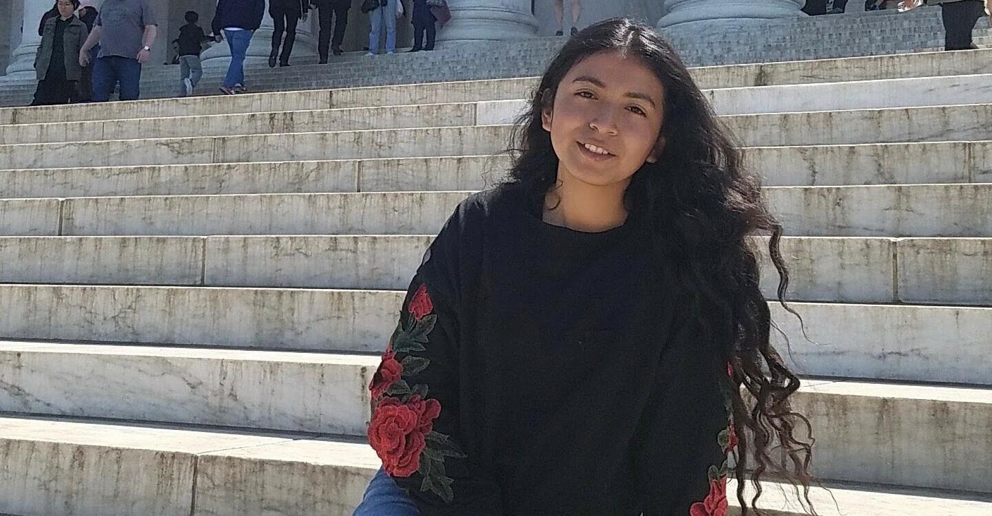 Samantha-Lee poses sitting on marble stairs in blue jeans and a black long-sleeve shirt