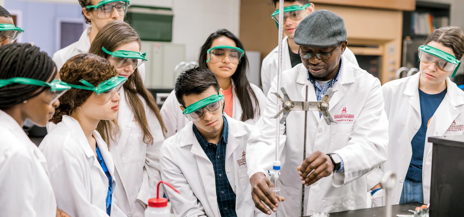 A professor begins to set up an experiment as he explains the experiment to the nine students around him