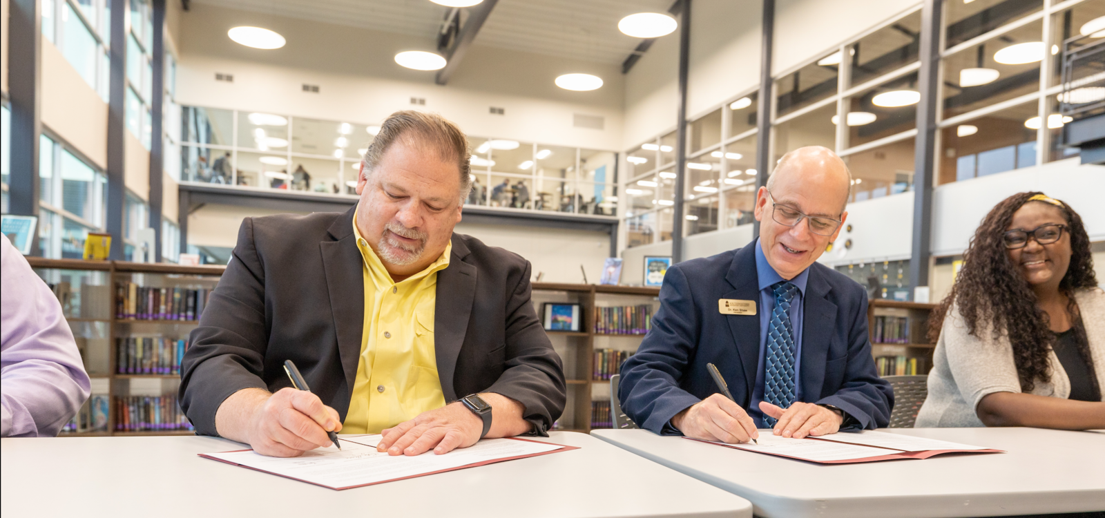 Dr. Shaw and another man sign papers on tables in a library