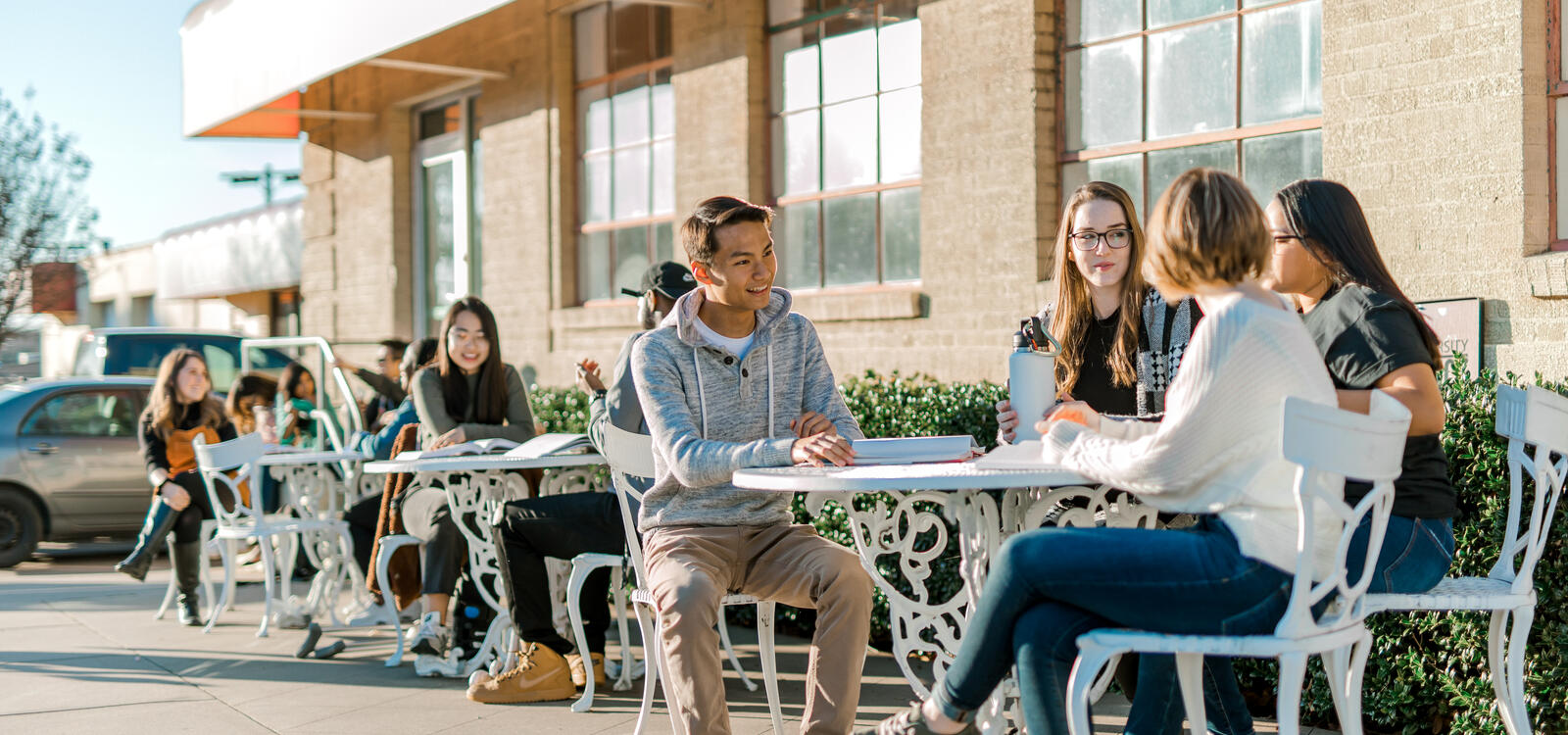 Outside several students are sitting with their friends at the metal tables and chairs outside of the Student Center