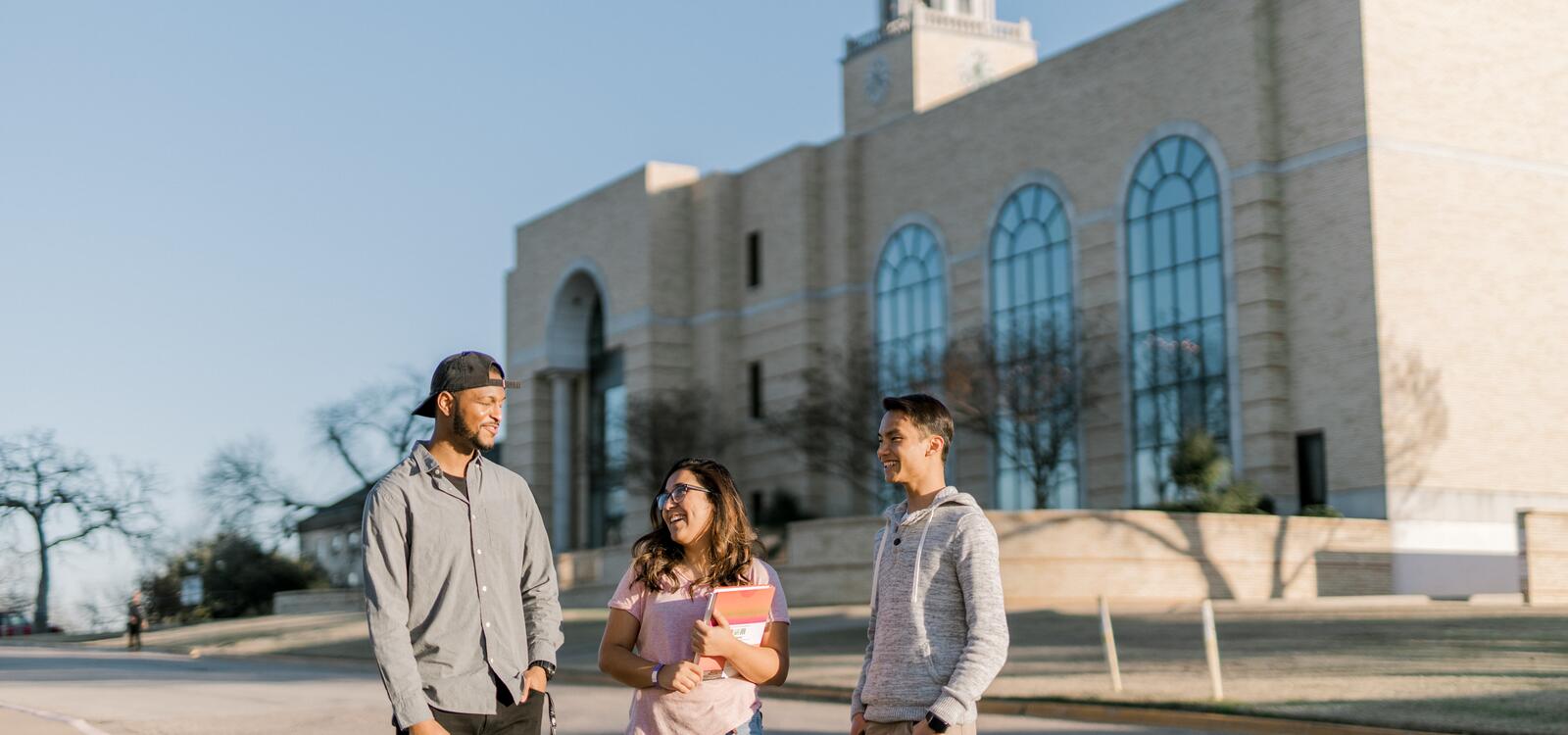 Standing outside in front of the library, three students stop to talk