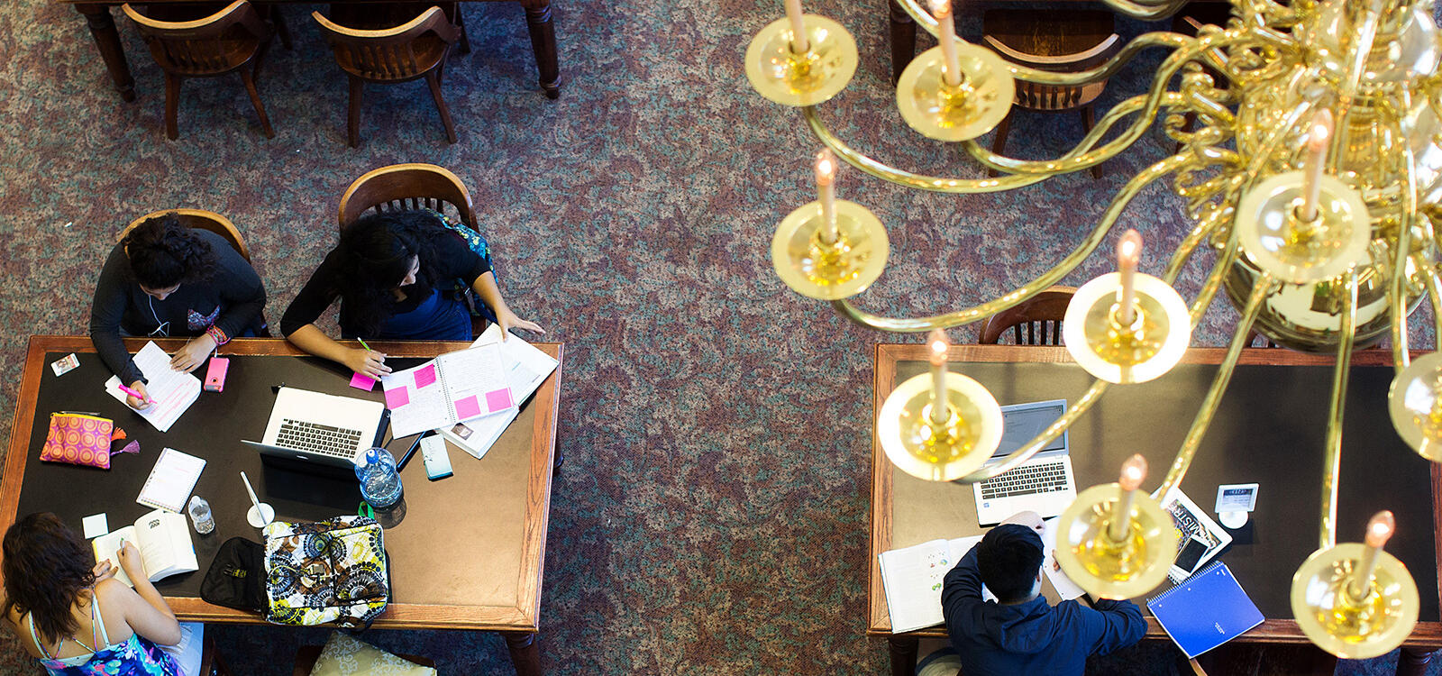 A birdseye view of students sitting at the library tables with their friends as they take notes and highlight their textbooks
