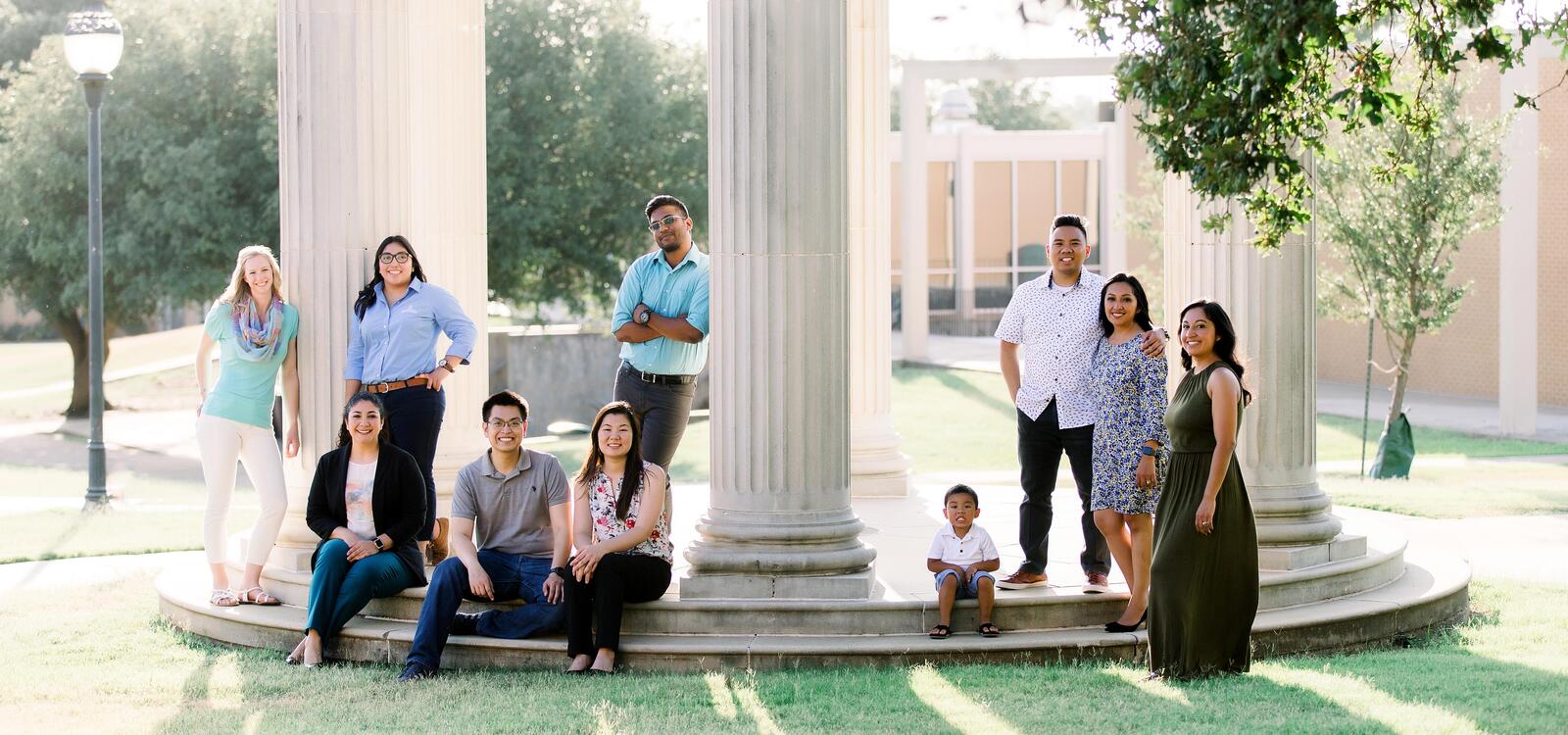 Around a white rotunda, different alumn smile as they stand and sit