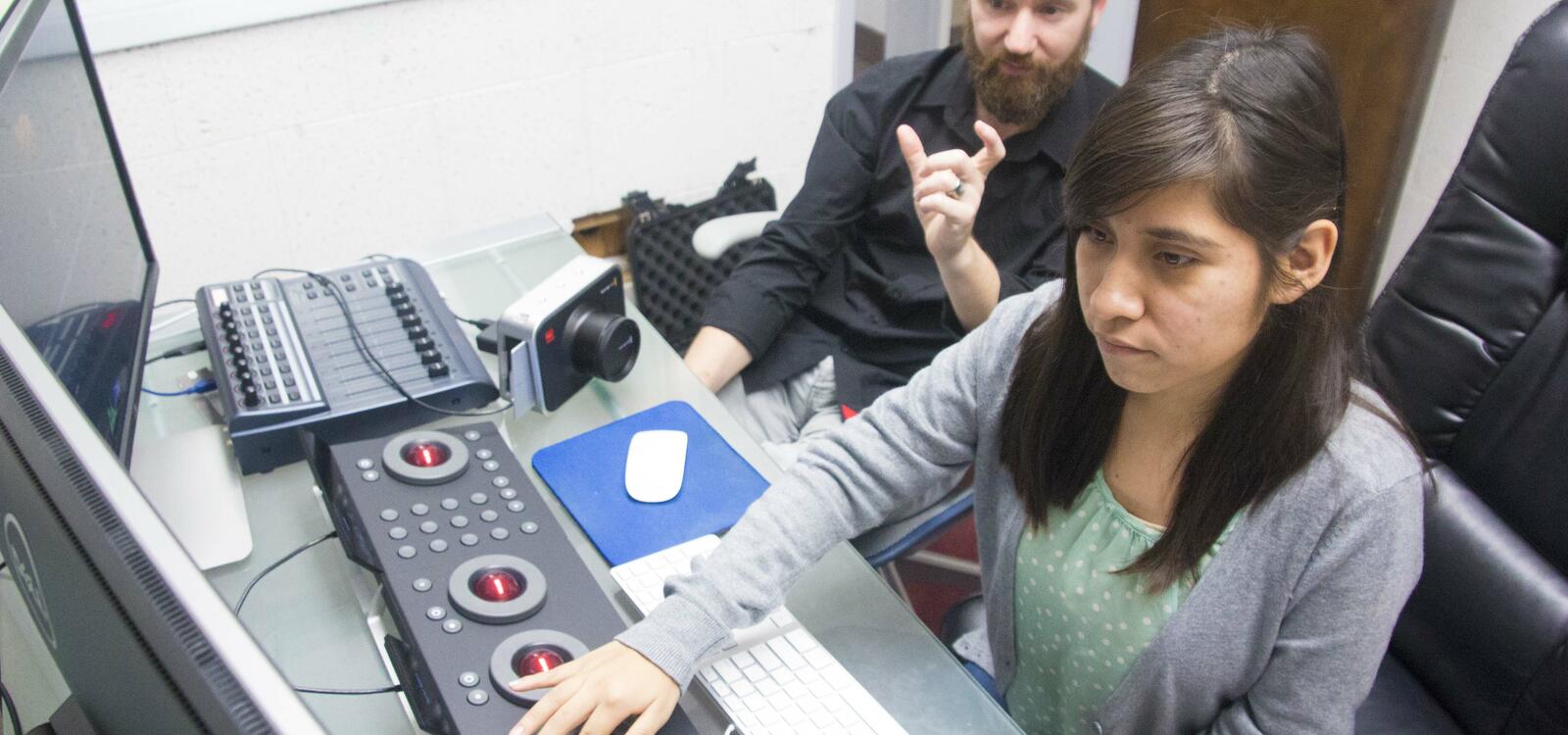 Sitting in front of a keyboard of buttons and balls, a student makes adjustments as she looks at two screens.