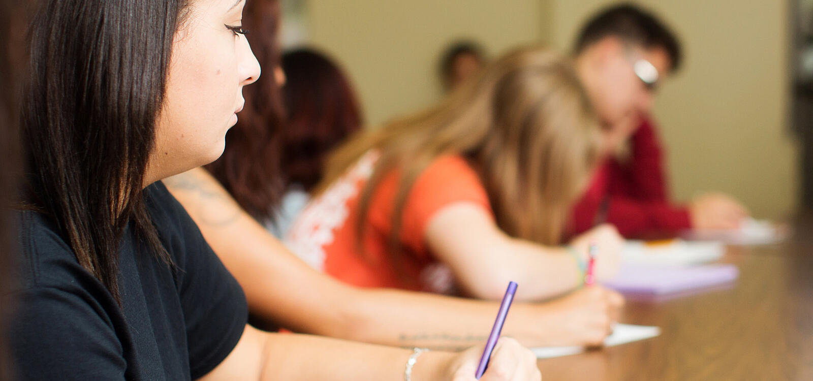 A female student sits with her peers as they all begin writing on their notepads