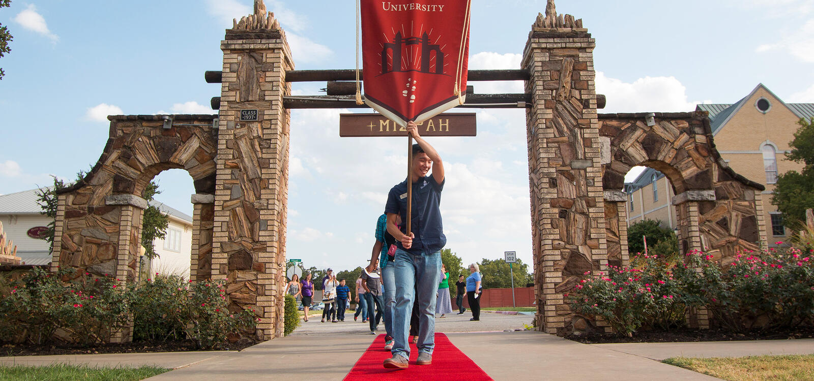 Student in front holds a SWAU banner as he leads incoming freshman down a red carpet through the Mizpah gate