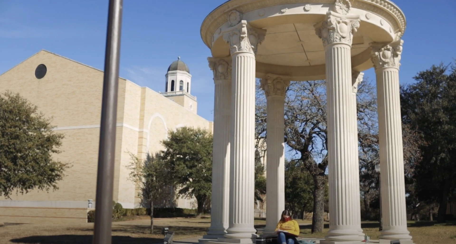 Student in yellow shirt sits at the rotunda with the library in the background