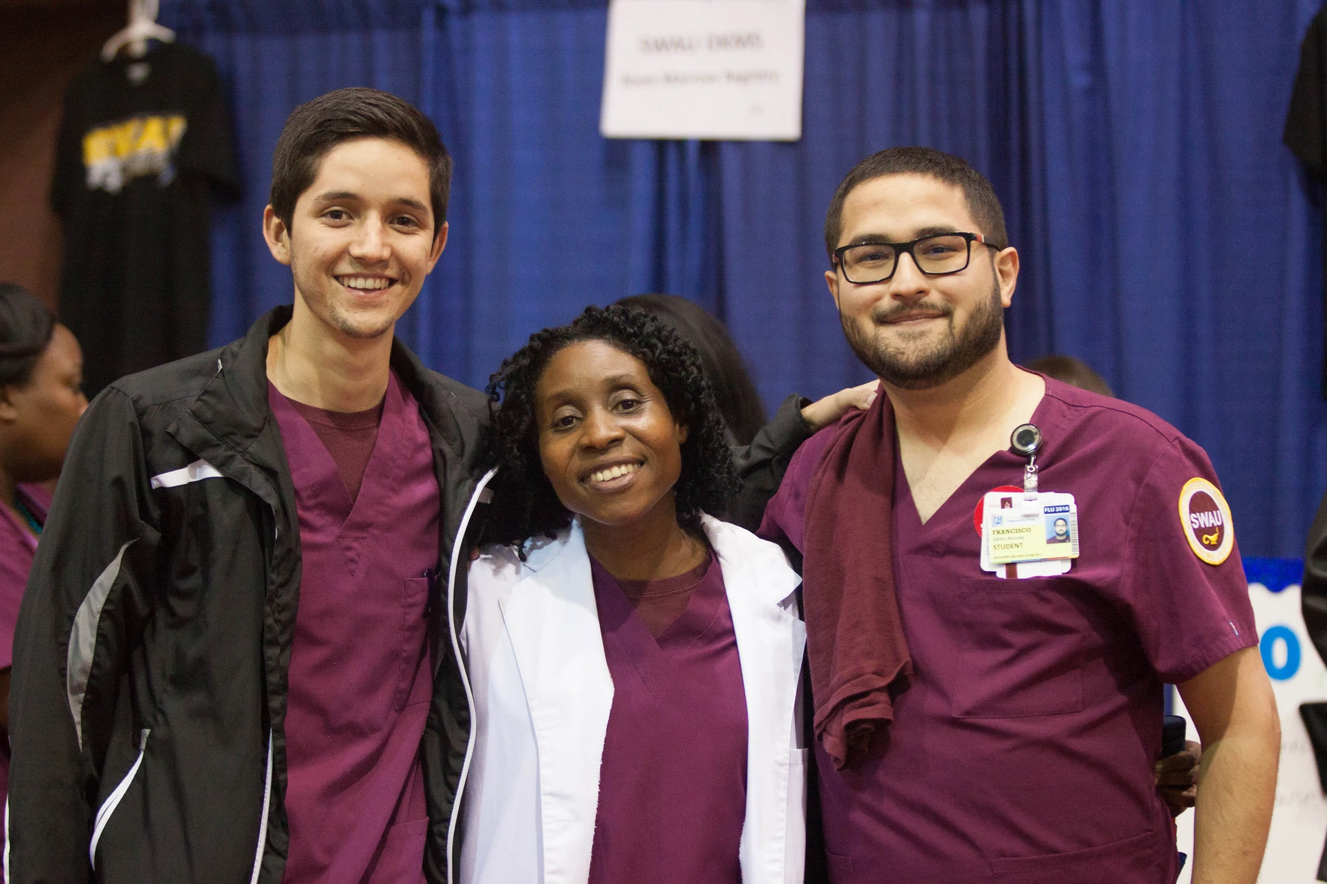 Three people dressed in SWAU scrubs pose in front of navy blue curtain