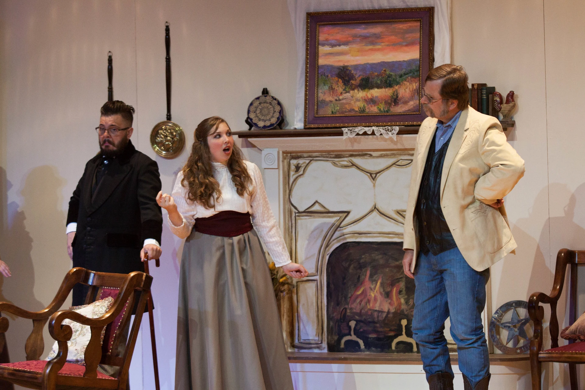 Three actors stand in front of a drawn fire place as they stand in their costumes