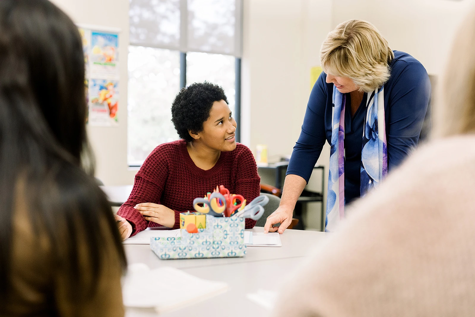 A professor leans over as she explains something to a student who is sitting