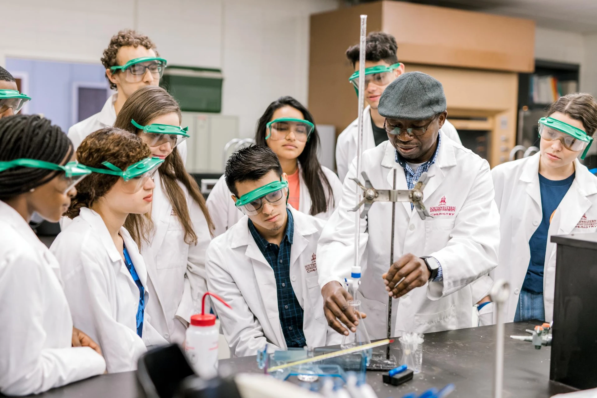 A professor begins to set up an experiment as he explains the experiment to the nine students around him