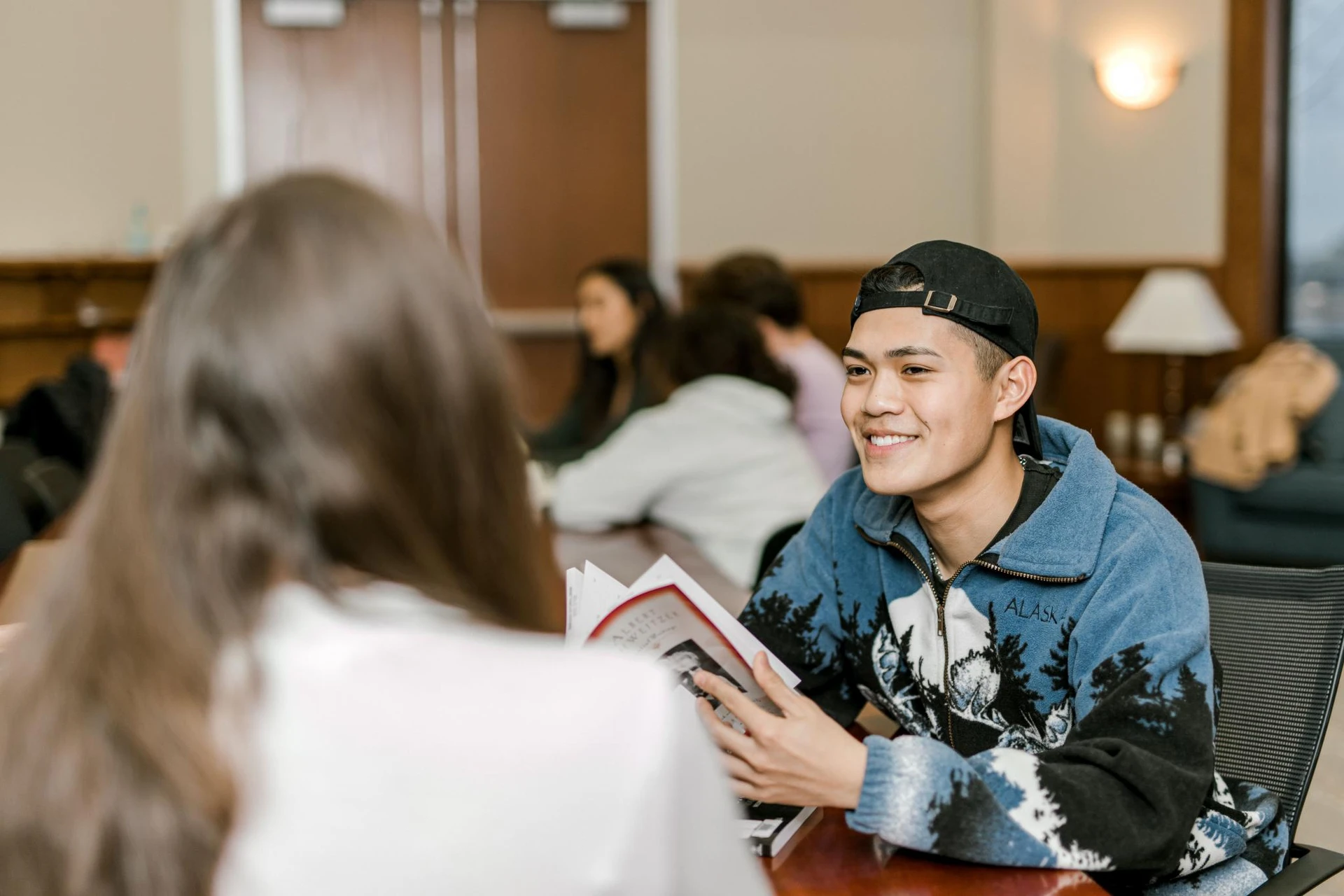 A student smiles as he talks to his peer sitting across from him