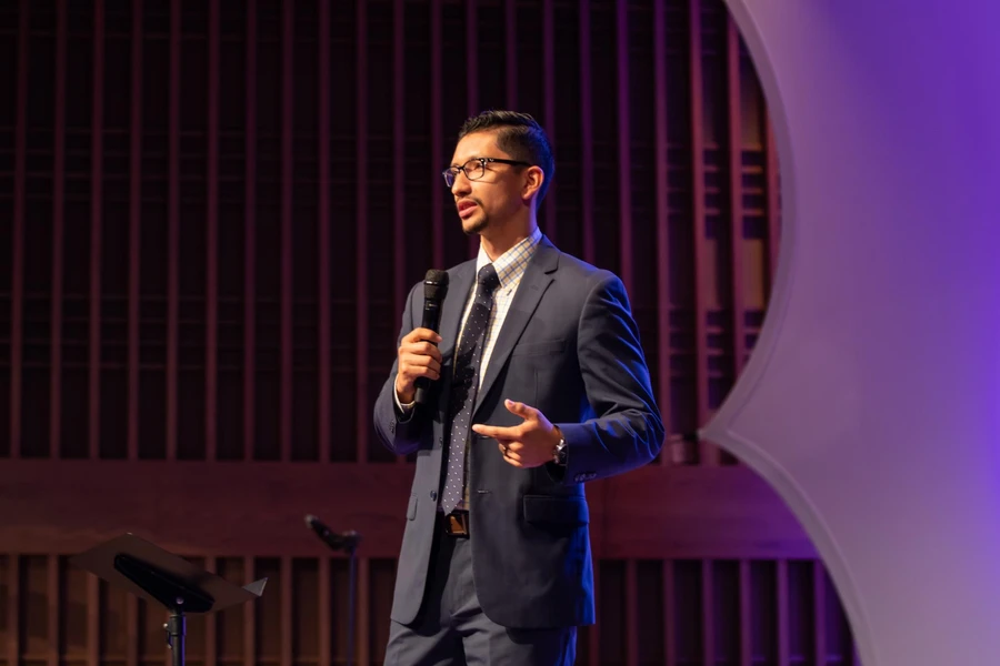 Pastor in blue suit wearing glasses and holding a mic as he speaks on the stage at church