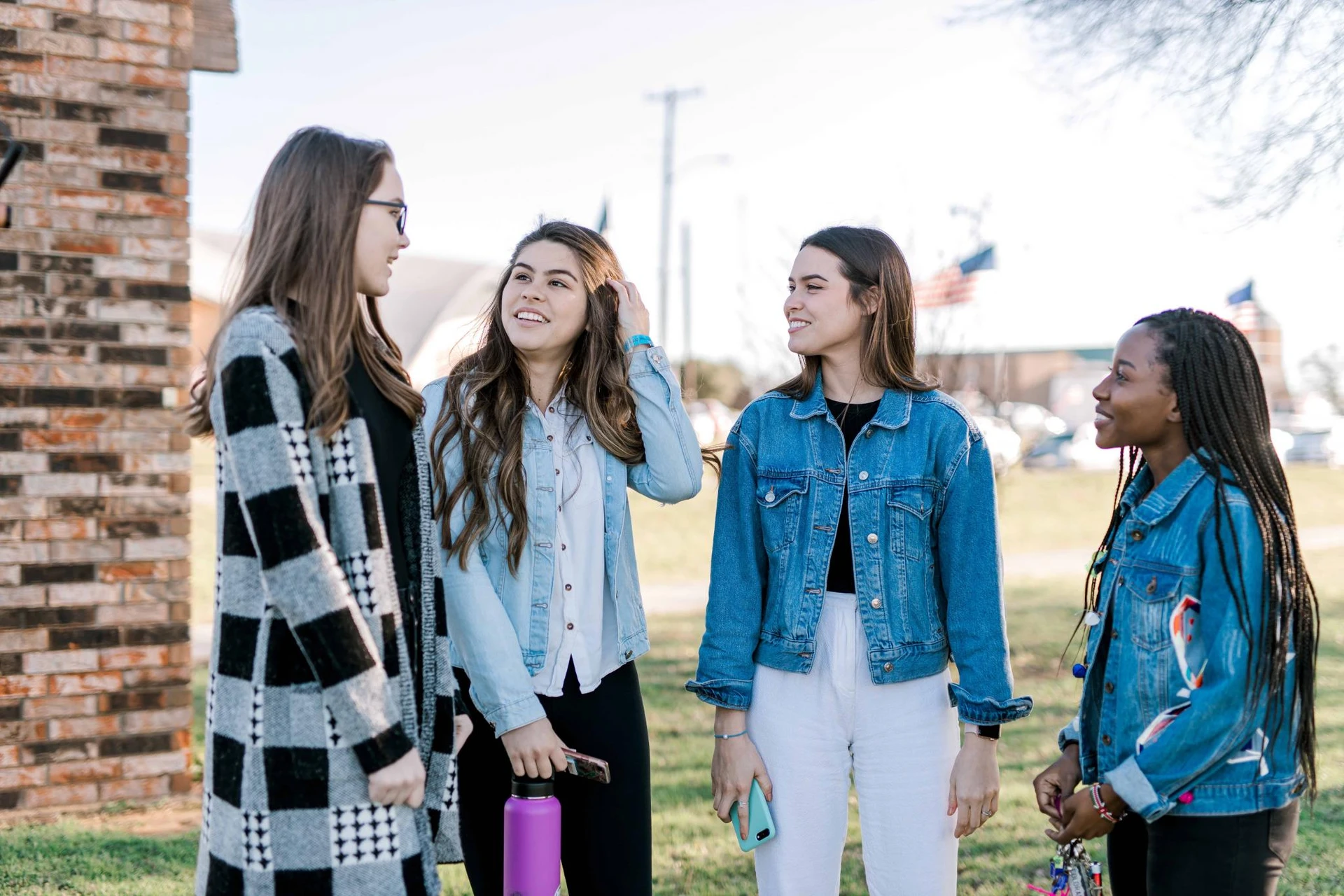 Four female students standing outside of a building smiling at each other.