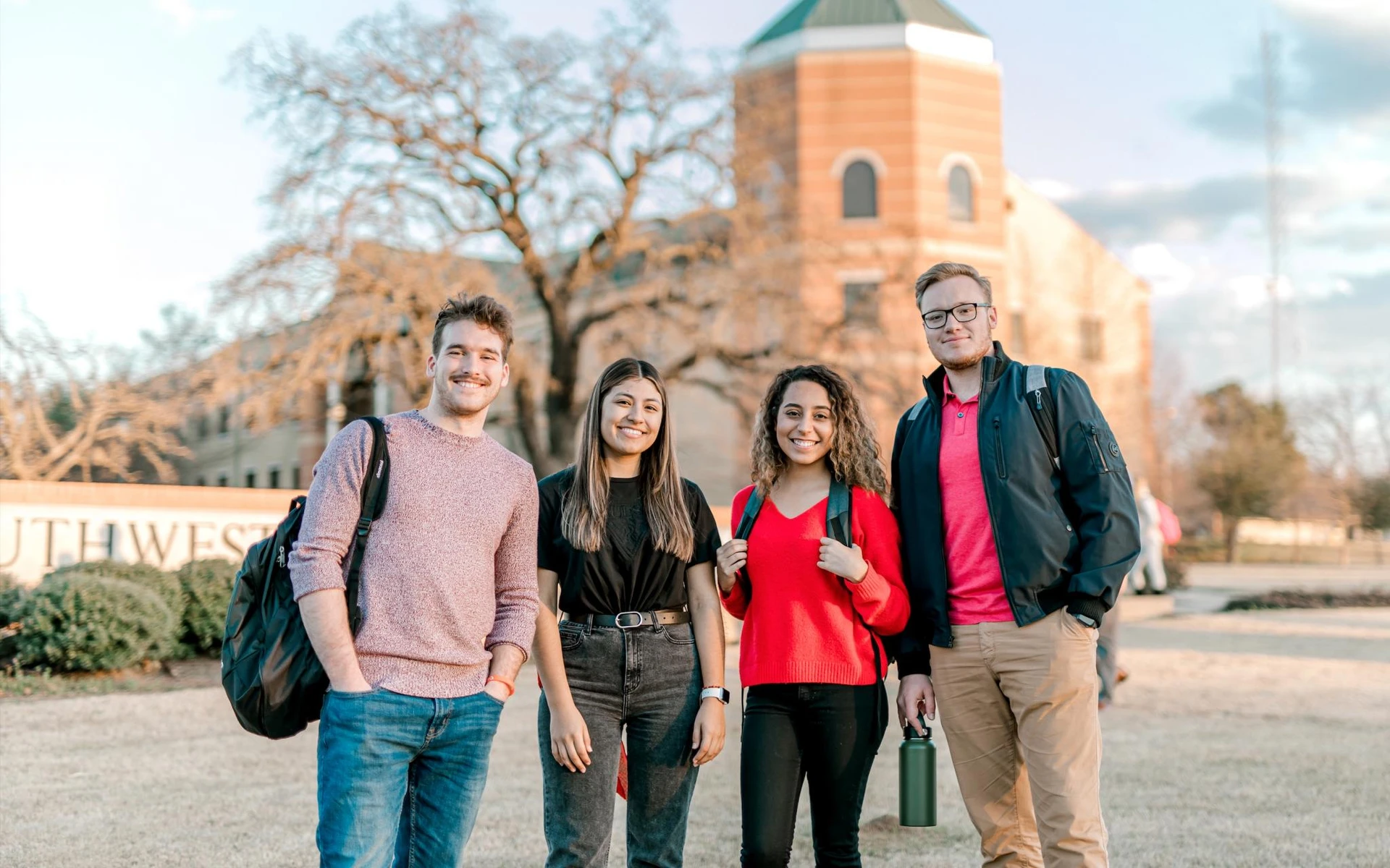 Four smiling adventist students look at the camera in front of Southwestern Adventist University