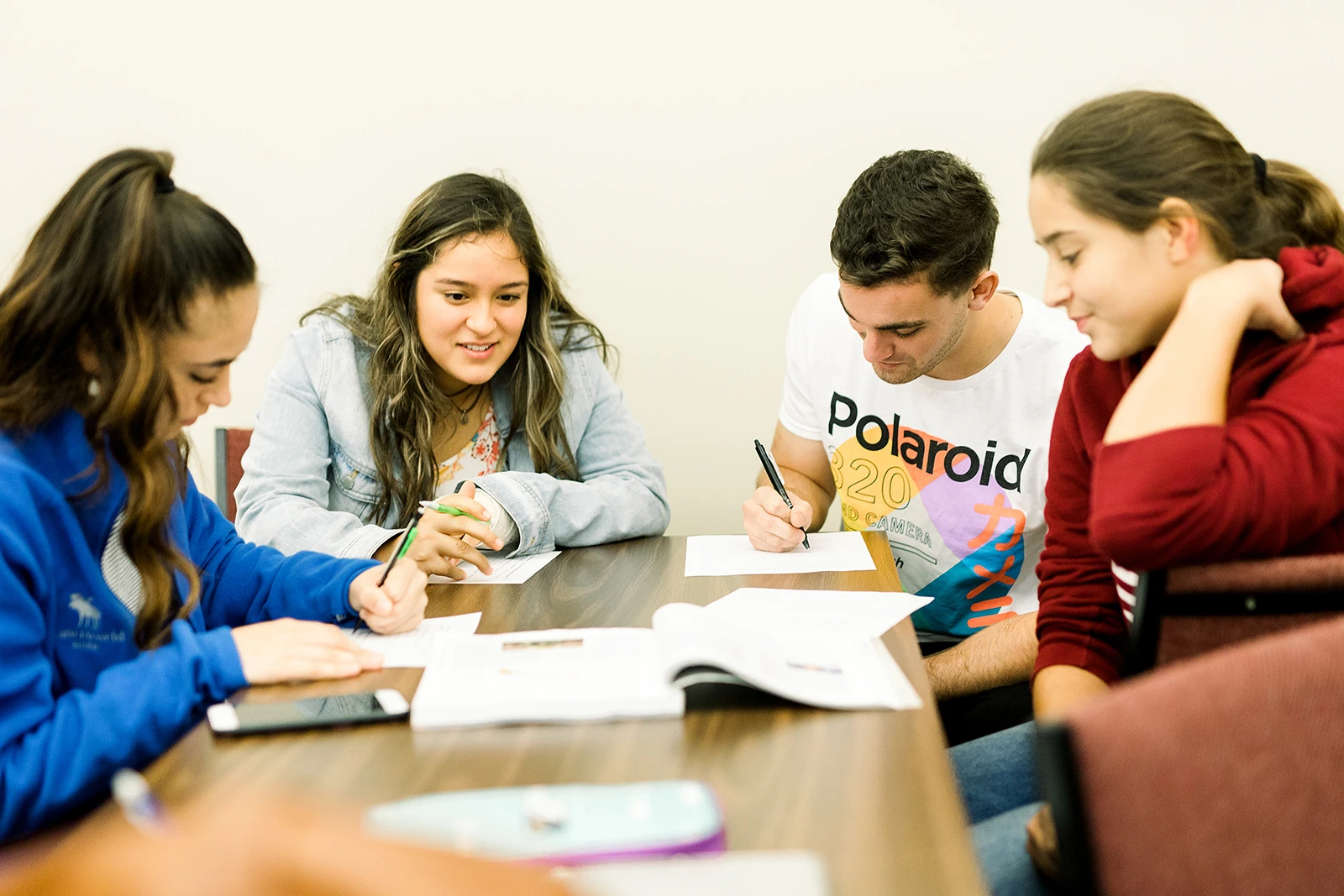 Four students sit together at a table and do assignments and study together