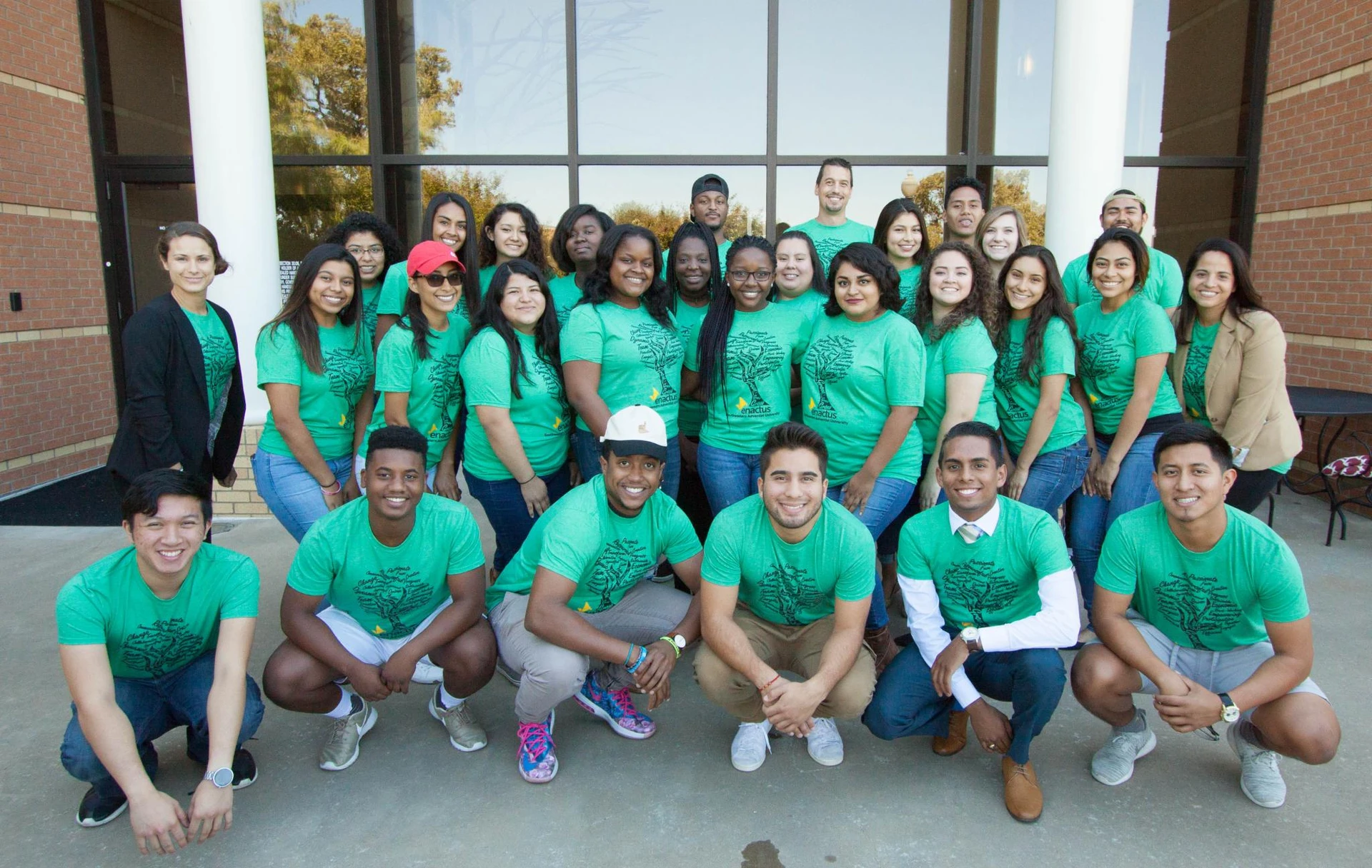 Dressed in matching green t-shirts, a group students stand in four rows and smile