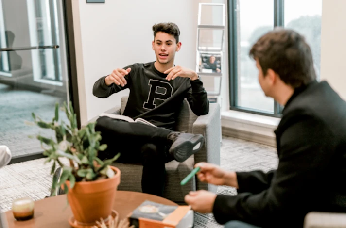 A male student, wearing a black crewneck, talks to his peers