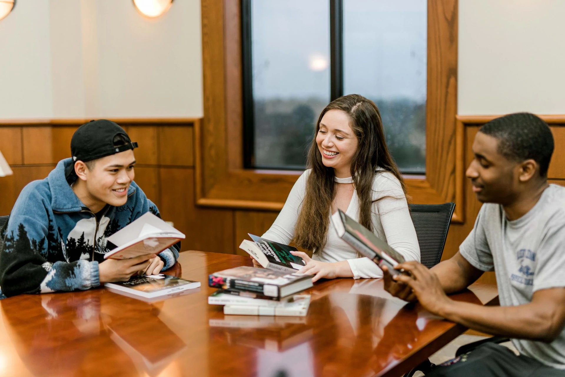 Three students sit together in a table in pechero smiling and looking through books