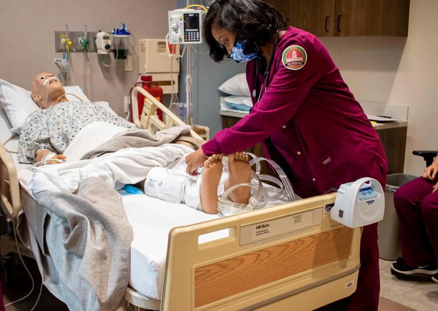 Female nursing student in a mask working near the feet of a mannequin 